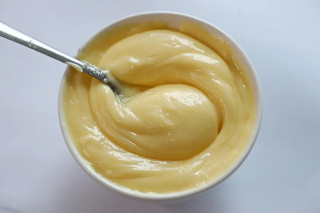 A white bowl of mayonnaise made by the Mueller immersion blender with a stainless steel spoon inside. 
