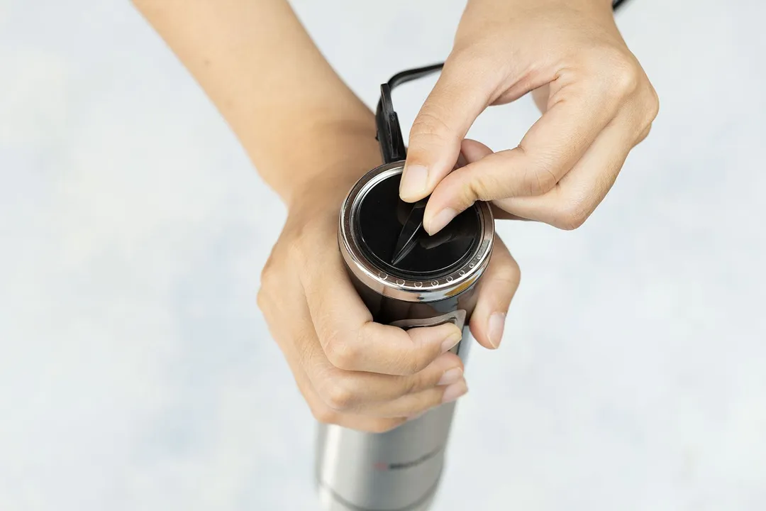 Someone uses two hands to control the Mueller Ultra-Stick immersion blender: one for holding the handle and pressing the power button at the same time, the other for rotating the speed dial.