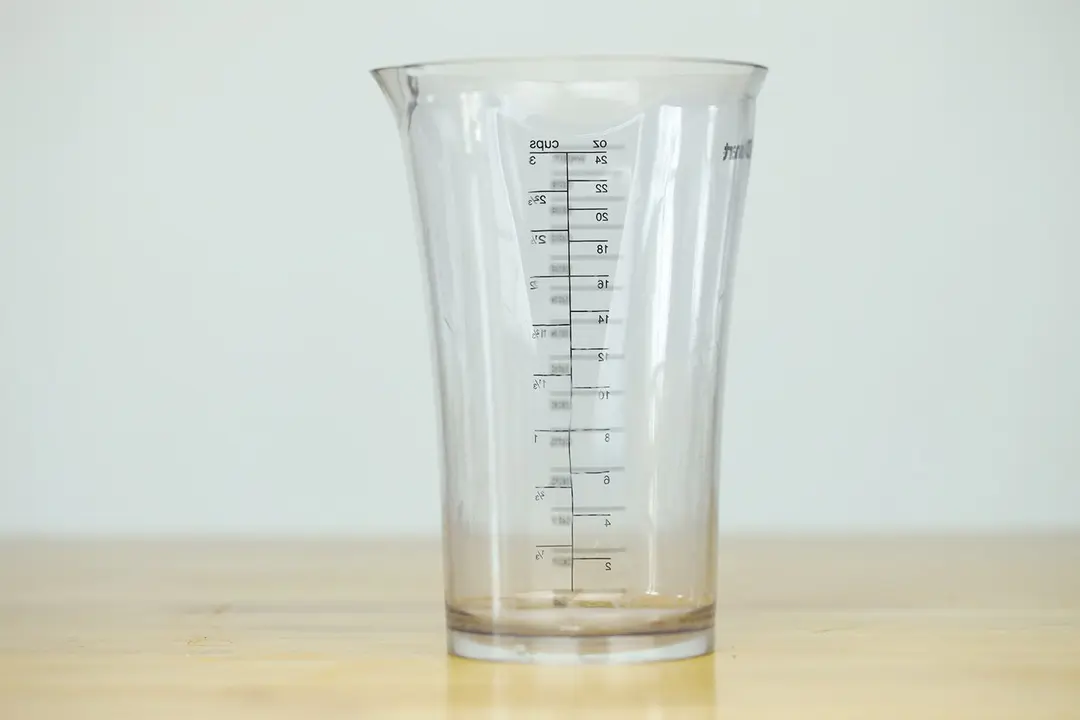 A 24-oz plastic beaker of the Cuisinart Smart stick standing on a yellow table.