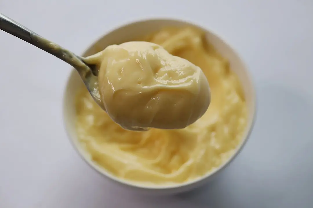 Scooping a spoon of mayonnaise from a full batch emulsified in a white bowl by the Cuisinart Smart Stick hand blender. 