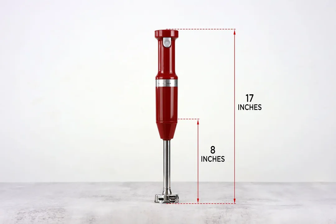 The KitchenAid cordless hand blender standing on top of its blending shaft on a gray table, with the length of the blending shaft being noted to the side as 8 inches, and the total length of the unit as 17 inches.