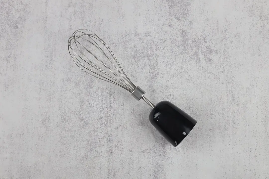 A whisk attachment of the BELLA hand-held blender lying flat on a gray table. 