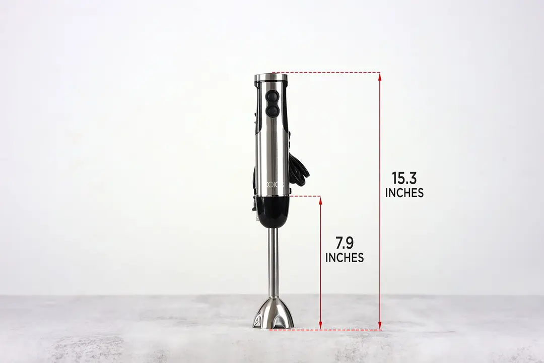 The KOIOS 4-in Immersion Blender stands on top of its blending shaft on a gray table, with the length of the blending shaft being noted to the side as 7.9 inches, and the total length of the unit as 15.3 inches. 