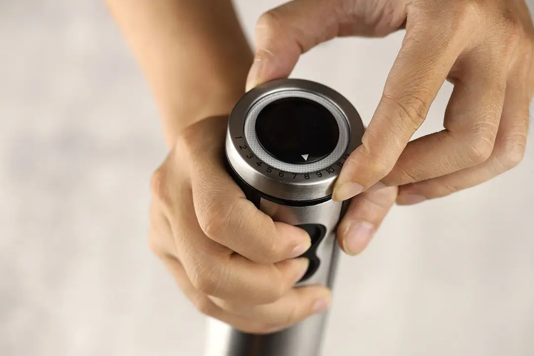Someone uses two hands to control the KOIOIS immersion blender: one for holding the handle and pressing the power button at the same time, the other for rotating the speed dial. 