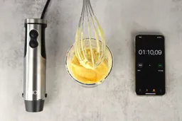 A little bit of mayonnaise sticking in the whisk attachment of the KOIOS 4-in-1 hand blender when it is removed from the full batch emulsified in a plastic beaker standing between the motor body and a smartphone displaying the total emulsion time (1 minute and 10 seconds). 