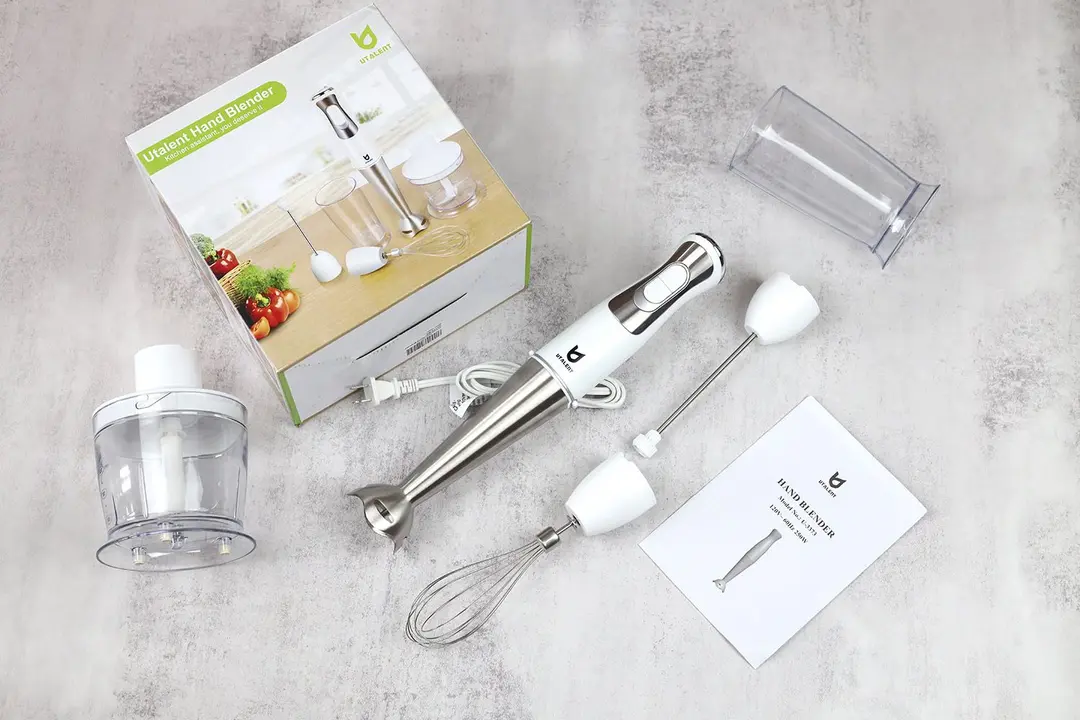 A user’s manual, plastic beaker, whisk attachment, blending wand with its motor body attached, milk frother attachment, food processor, and paper carton box of the UTALENT Immersion Blender lying side by side on a gray table.