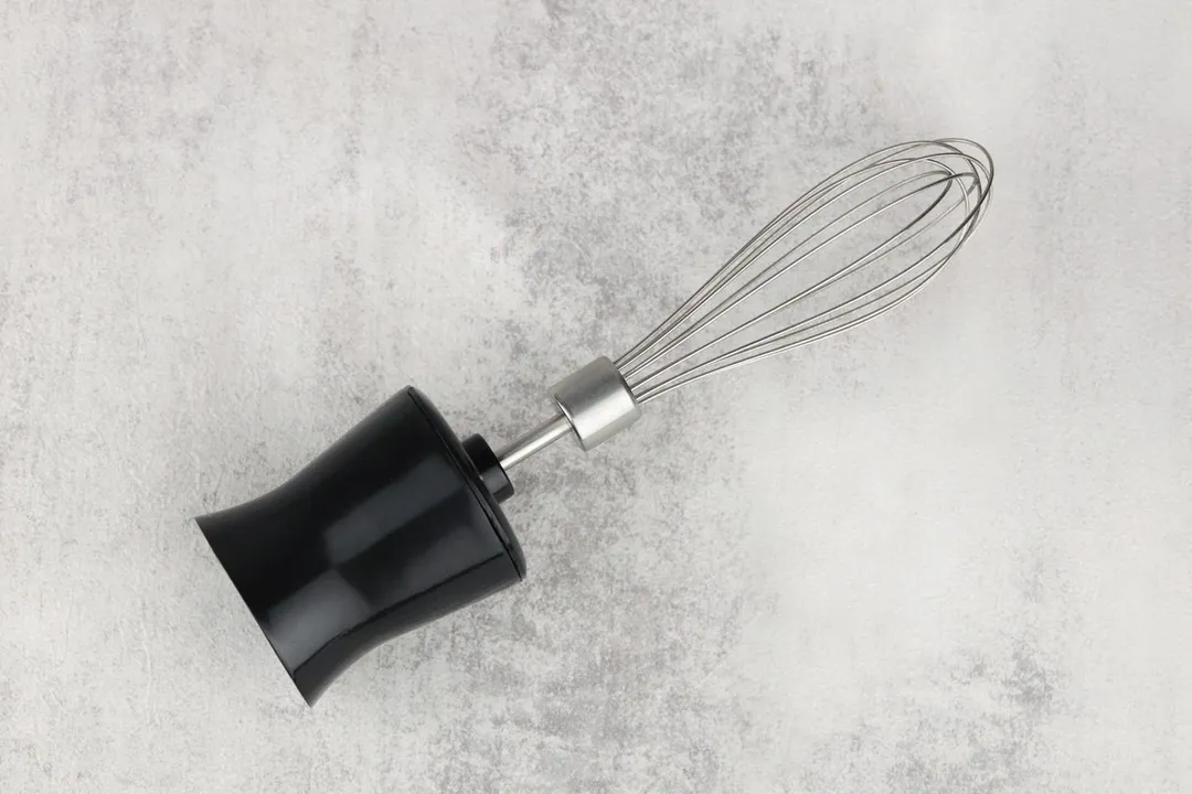 A whisk attachment of the Hamilton Beach stick blender lying flat on a gray table.