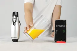 Someone is holding a plastic beaker which contains a batch of failed mayonnaise of the Hamilton Beach immersion blender and is between the motor body and a smartphone displaying the total emulsifying time (2 minutes and 8 seconds).