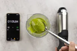 Scooping a spoon of smoothie from the plastic beaker to check its texture after the Vitamix immersion blender had completed the test in 1 minute and 5 seconds. 