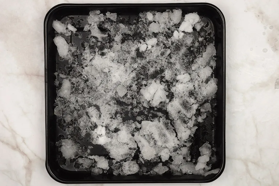 A black tray of coarse crushed ice on a table.