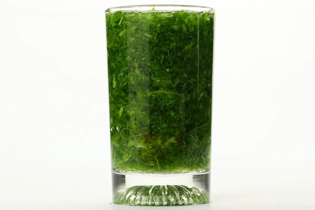 A glass of water with fibrous green pulp produced by the Hamilton Beach personal blender.