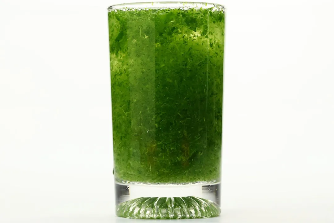 A glass of water with fibrous green pulp produced by the KOIOS personal blender.