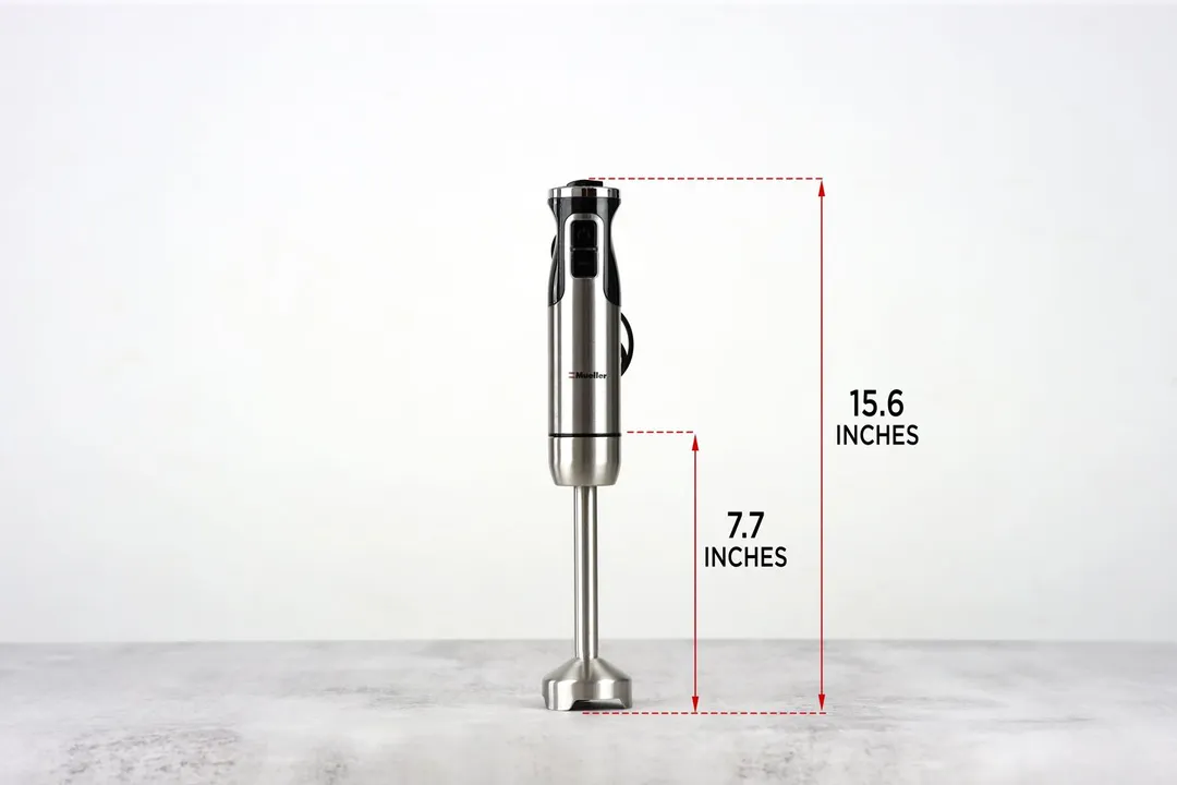 The Mueller Austria Ultra-Stick Immersion Blender standing on top of its blending shaft on a gray table, with the length of the blending shaft being noted to the side as 7.7 inches, and the total length of the unit as 15.55 inches.