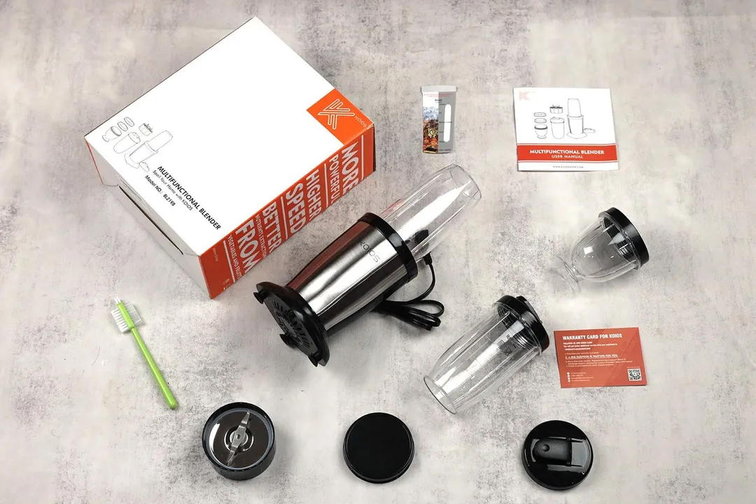 The KOIOS Bullet personal blender lying on a table with its accessories, including two lids, two additional blending cup with lids, a paper carton box, an additional blade assembly, a cleaning brush, and a user guide.