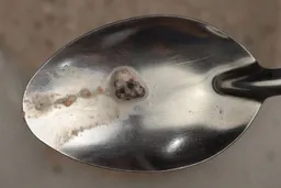 A tiny unblended chunk of dried blueberry left behind by the Ninja QB3001SS Fit personal blender on a stainless steel spoon.