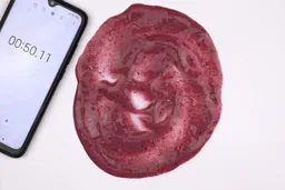 To check for solid chunks, after finishing blending, the fruity smoothie made by the Nutribullet Pro Nutrient Extractor being spread throughout a white paper with a smartphone displaying the total blending time (50 seconds) next to its.