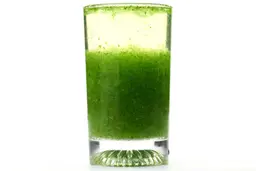 A glass of water with fibrous green pulp produced by the Black+Decker Fusionblade Personal Blender sinking from its top to bottom.