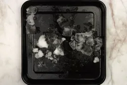 A black tray of crushed ice produced by the Black+Decker Fusionblade 12-Speed Personal Blender being on a table. 
