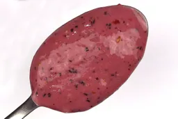 A spoon of fruity smoothie packed with blueberries, blackberries, strawberries, and mango made by the Oster portable blender with a smartphone displaying the total blending time ( 1 minute and 40 seconds) next to it.