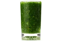 A glass of water with fibrous greens pulp produced by the Oster Single-Serve Blender.