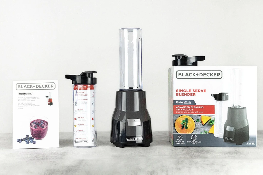 The Black+Decker Fusionblade Personal Blender standing on a white table with its accessories, including a to-go lid, an extra blending cup with lid, a user’s manual, and a paper carton box, by its sides.