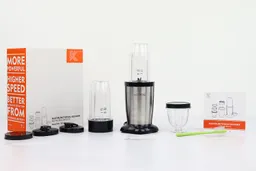 The KOIOS Bullet personal blender standing on a table with its accessories, including three lids, an additional blending cup with blade assembly attached, a paper carton box, a short cup with lid, a cleaning brush, and a user guide.