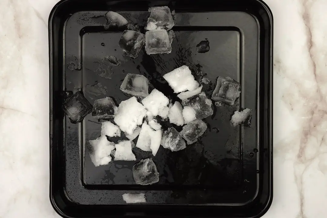 A black tray of ice cubes on a table.