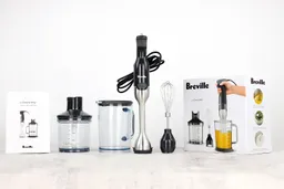 The Breville BSB510XL Immersion Blender is packed in a paper carton box with a motor body, blending shaft, wish attachment, food processor attachment, plastic beaker with lid, and a user’s manual.
