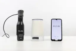 The plastic beaker containing testing beaten egg-white of the Breville immersion blender is put upside down on the white table with its motor body and a smartphone displaying the total whipping time (1 minute and 21 seconds) by its sides.