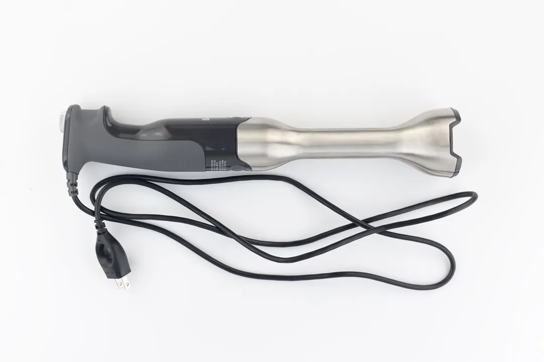 The Breville Immersion Blender on a white table with its power cord that features a 2-prong plug rolled up next to it.