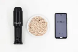 A white plate of almond pulp produced by the Chefman battery-powered stick blender being between the Chefman’s motor body and a smartphone displaying the total grinding time (55 seconds).