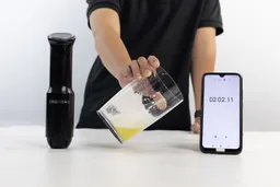 Someone is holding a plastic beaker which contains a batch of failed beaten egg-white of the Chefman immersion blender and is between the Chefman’s motor body and a smartphone displaying the total whipping time (2 minutes 2 seconds).