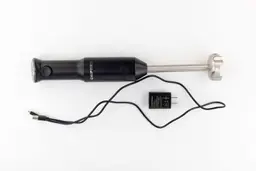 The Chefman Cordless Immersion Blender on a white table with its charger adapter and USB cord rolled up next to it.