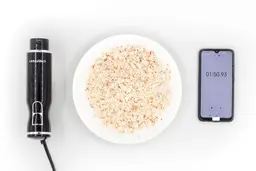 A white plate of almond pulp produced by the Chefman corded stick blender being between the Chefman’s motor body and a smartphone displaying the total grinding time (1 minute and 50 seconds).