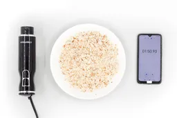 A white plate of almond pulp produced by the Chefman corded stick blender being between the Chefman’s motor body and a smartphone displaying the total grinding time (1 minute and 50 seconds).