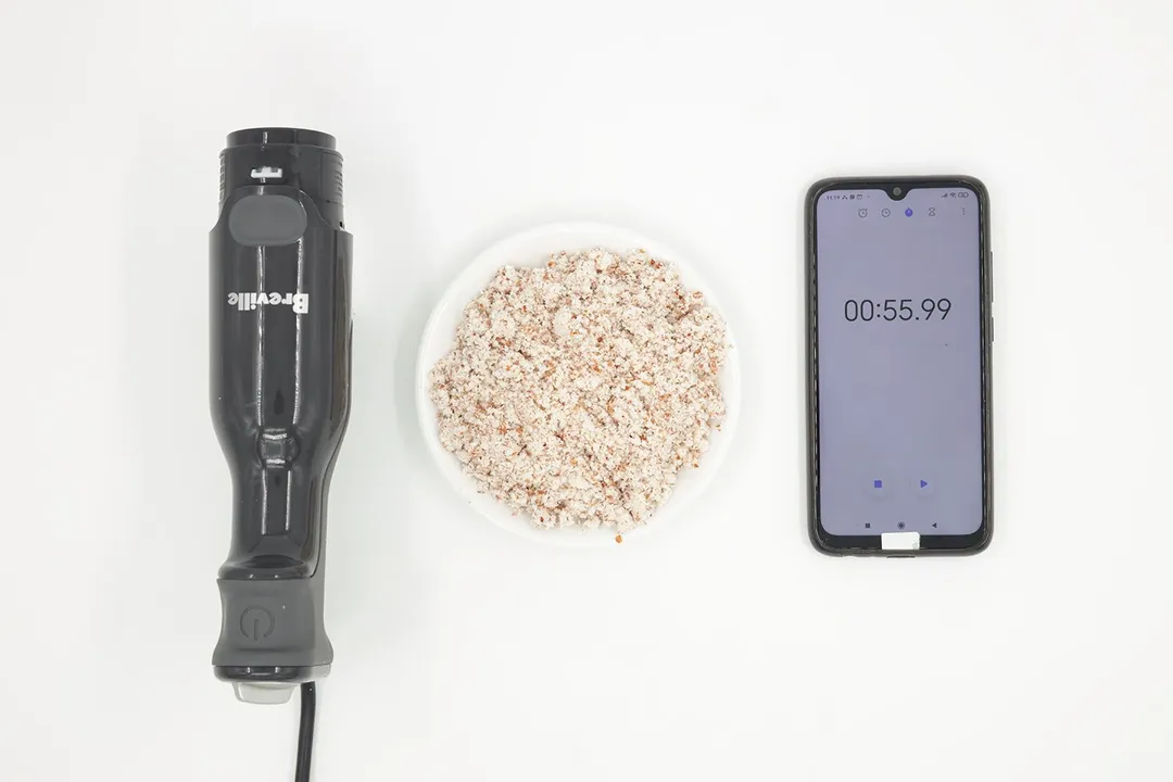 A white plate of almond pulp produced by the Breville stick blender being between the Breville’s motor body and a smartphone displaying the total grinding time (55 seconds).
