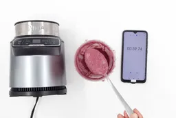 A spoon of fruity smoothie packed with blueberries, blackberries, strawberries, and mango made by theNinja BN401 Nutri Pro blender with a smartphone displaying the total blending time ( 59 seconds) next to it.