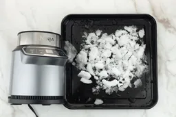A black tray of crushed ice produced by the Ninja BN401 Nutri Pro Personal Blender being on a table.