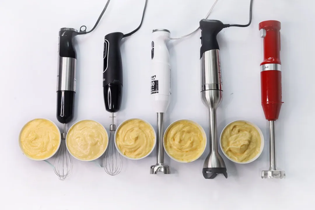 Five immersion blenders lying on a white table with their testing mayonnaise by their side.