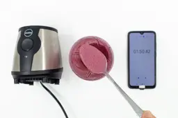 Scoping a spoon of fruity smoothie from a plastic cup that is standing between the iCucina personal blender and a smartphone displaying the blending time (1 minute and 50 seconds)