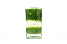 A glass of water with fibrous green pulp produced by the iCucina Personal Blender sinking from its top to bottom.
