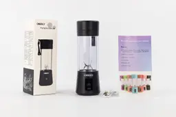 The OBERLY personal blender standing on a white table with a user’s manual, charging cable, and paper carton box by its sides.