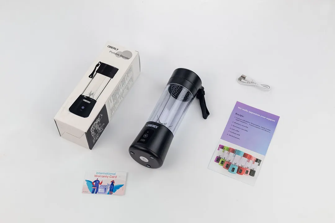 The OBERLY personal blender lying on a table with a paper carton box, user guide, and warranty card by its sides.