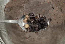 Using a spoon to scoop fruit chunks from a mesh strainer containing protein shake produced by the La Reveuse. 