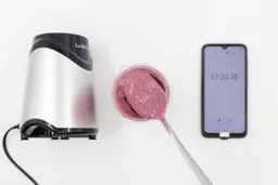 A spoon of fruity smoothie packed with blueberries, blackberries, strawberries, and mango made by the La Reveuse portable blender with a smartphone displaying the total blending time ( 1 minute and 20 seconds) next to it. 