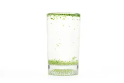 A glass of water with fibrous green pulp produced by the La Reveuse sinking from its top to bottom. 