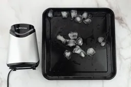 A black tray of crushed ice produced by the La Reveuse Personal Blender being on a table.