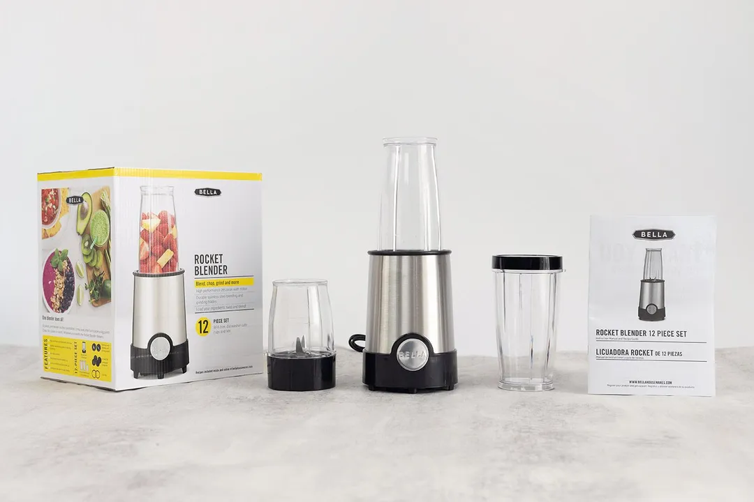 The BELLA personal blender standing on a table with its additional accessories, including two blending cups with lids, user’s manual, and paper carton box, by its sides.