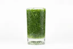 A glass of water with fibrous greens pulp produced by the BELLA Single-Serve Blender.
