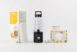 The PopBabies personal blender standing on a white table with a user’s manual, charging cable, funnel, ice cube tray, and paper carton box by its sides.